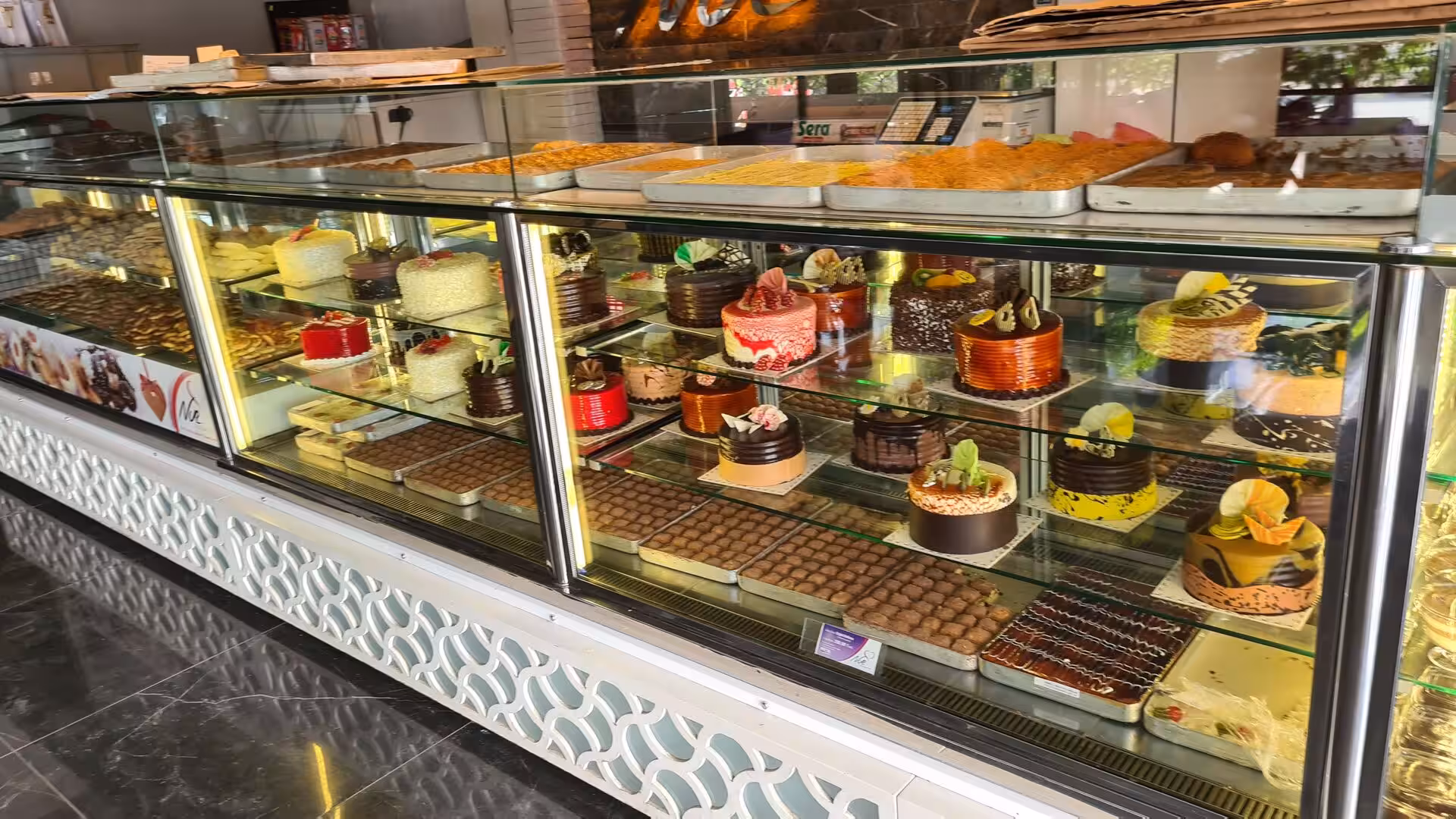 A glass bakery case presents an array of colorful cakes and sweets.