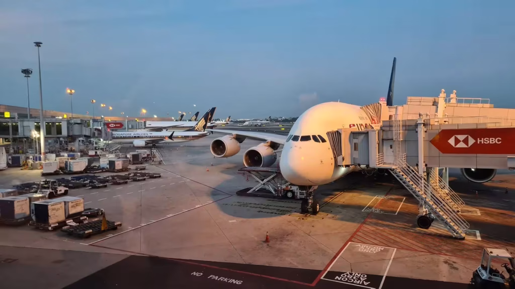 A massive double-deck airliner waits at a gate while other planes idle on the tarmac at dusk.