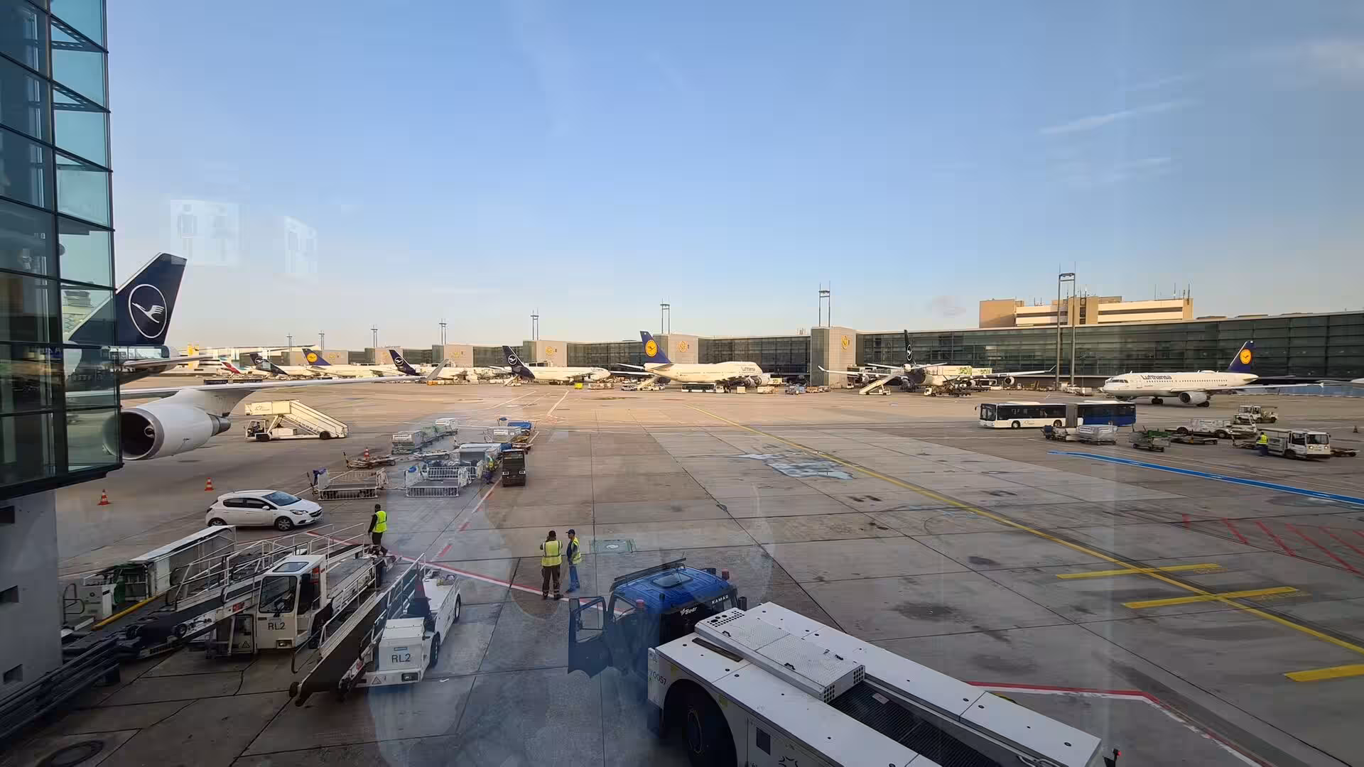 Lufthansa aircraft wait at their gates as ground crew work the apron at dusk.