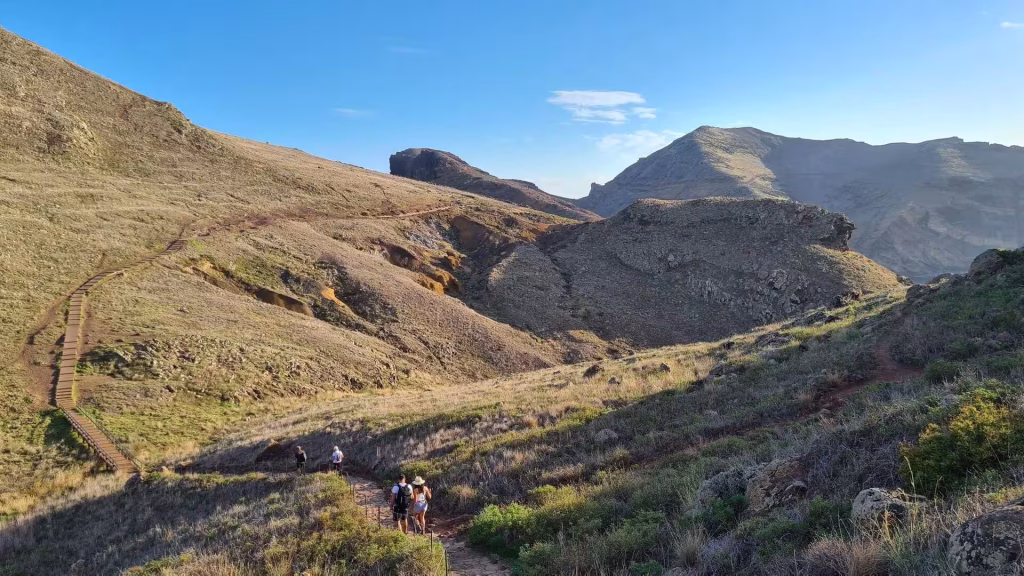 A wooden boardwalk winds down golden slopes where hikers follow the path.