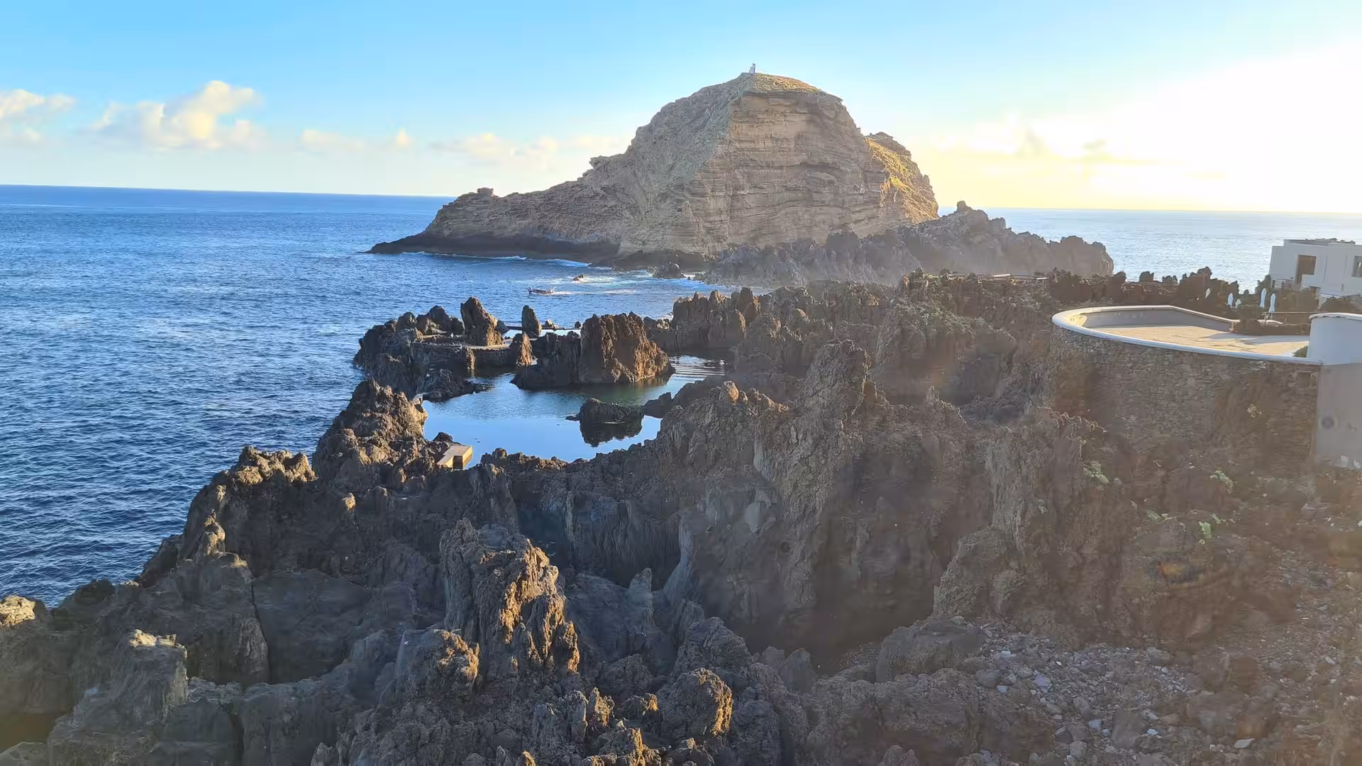 Rugged black lava rocks and a distant islet glow in warm evening light.