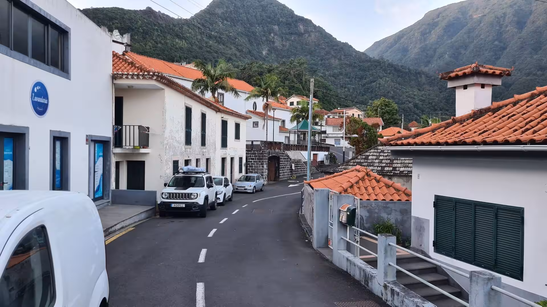 A quiet village lane lined with white houses and terracotta roofs beneath forested peaks.