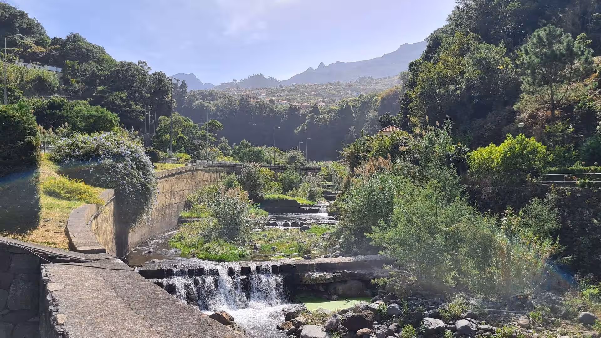 A small waterfall drops into a lush mountain ravine.