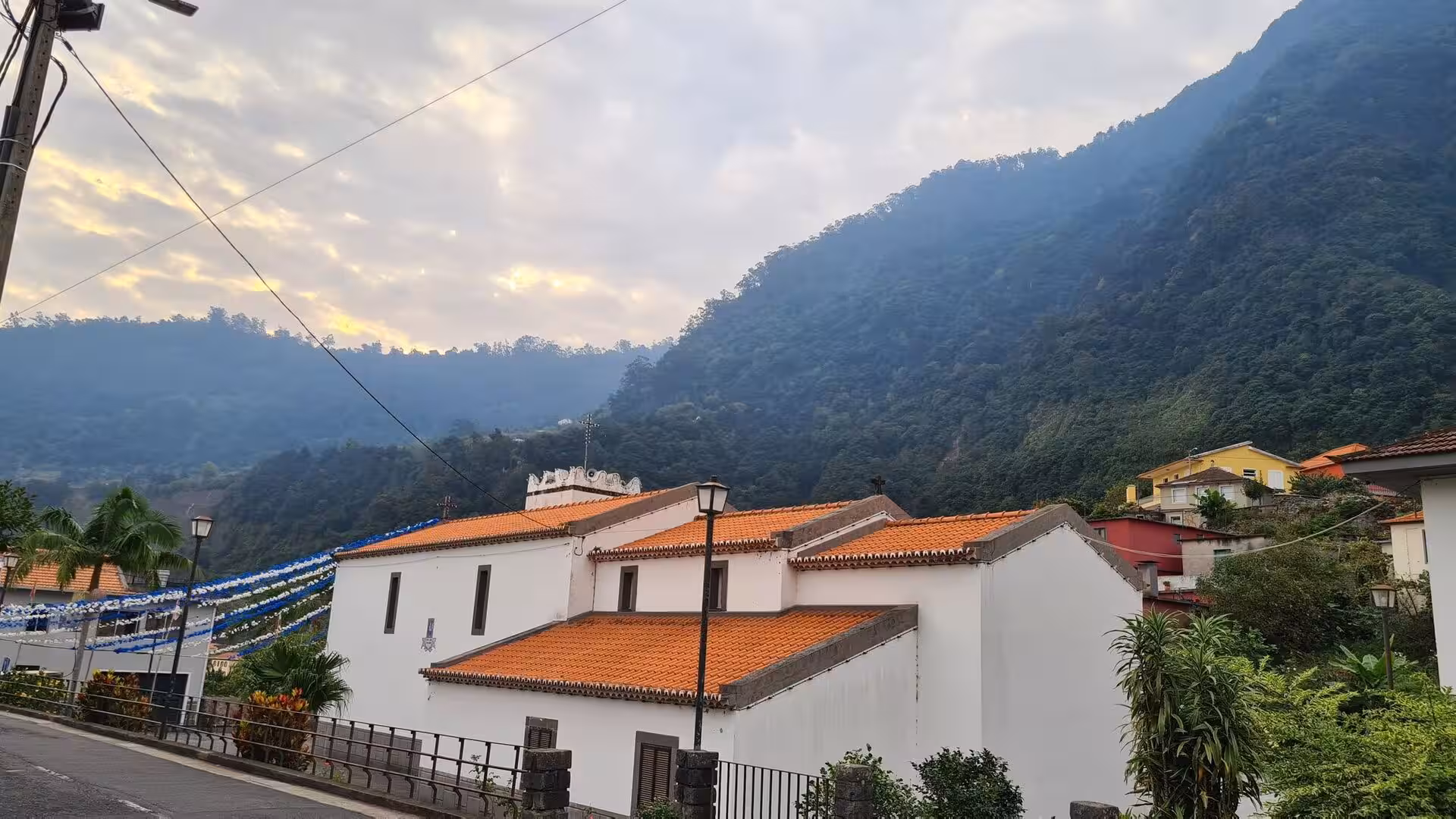 A white chapel with an orange roof stands against a steep dark mountain.