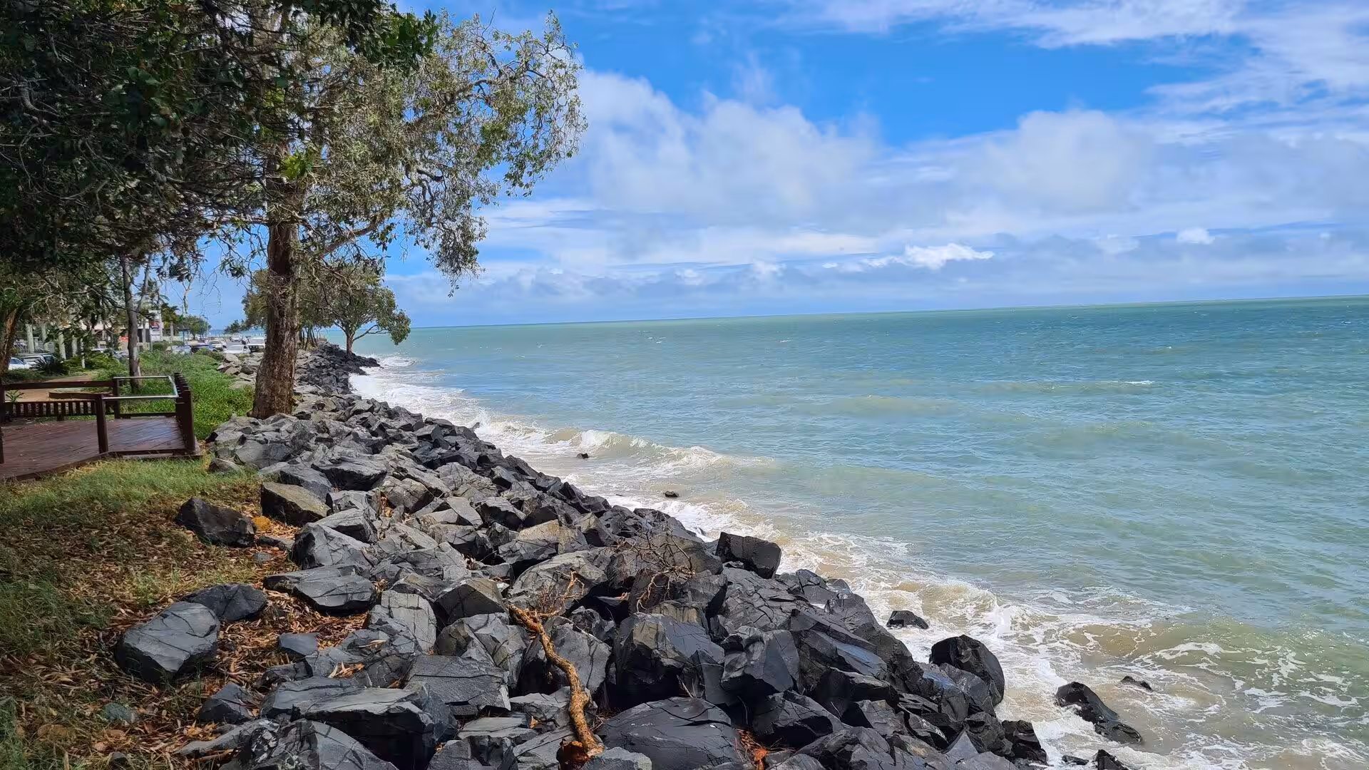 Large dark boulders line the shore where gentle waves meet turquoise water.