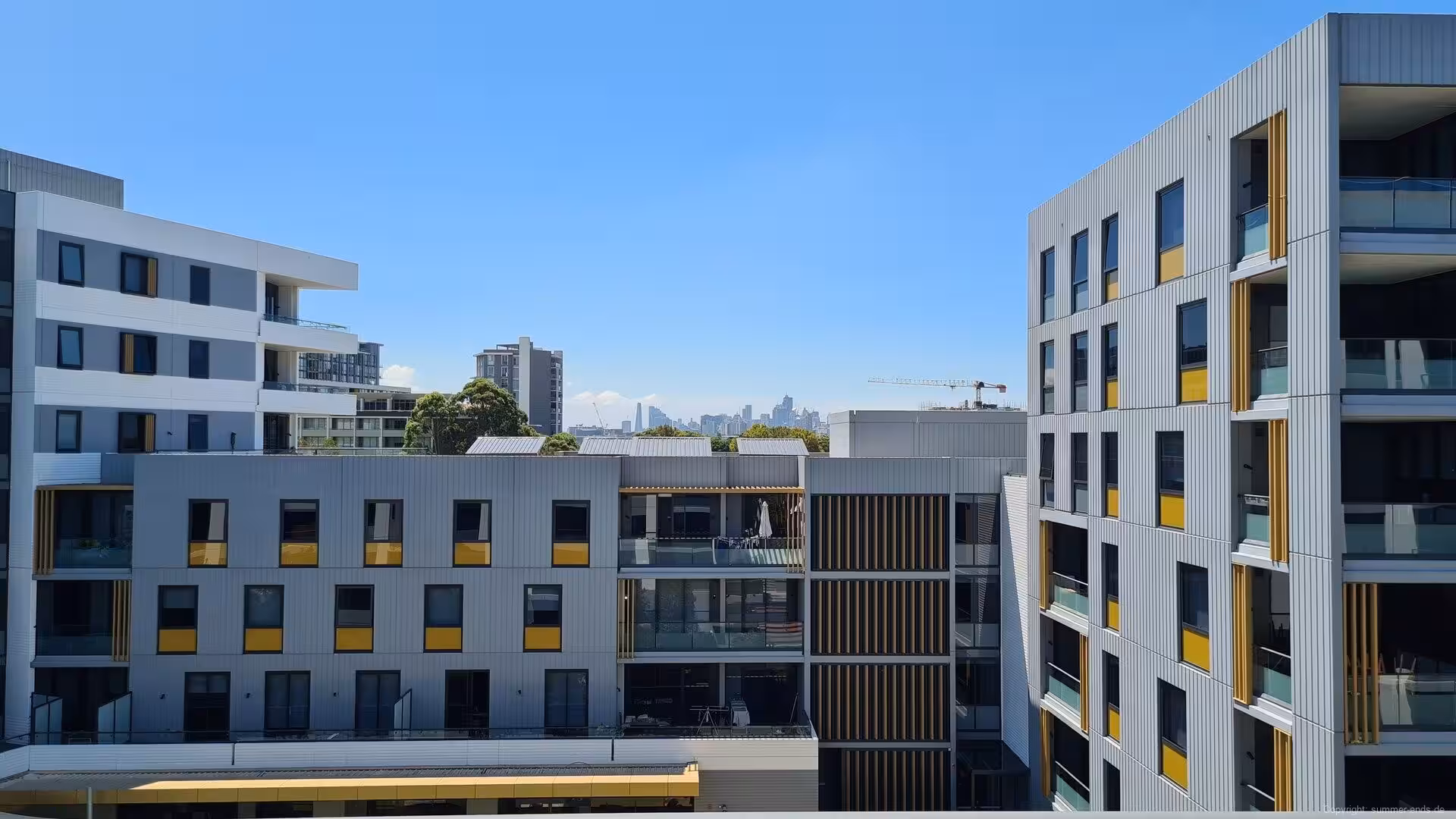 Grey apartment buildings with yellow accents frame a distant city skyline.