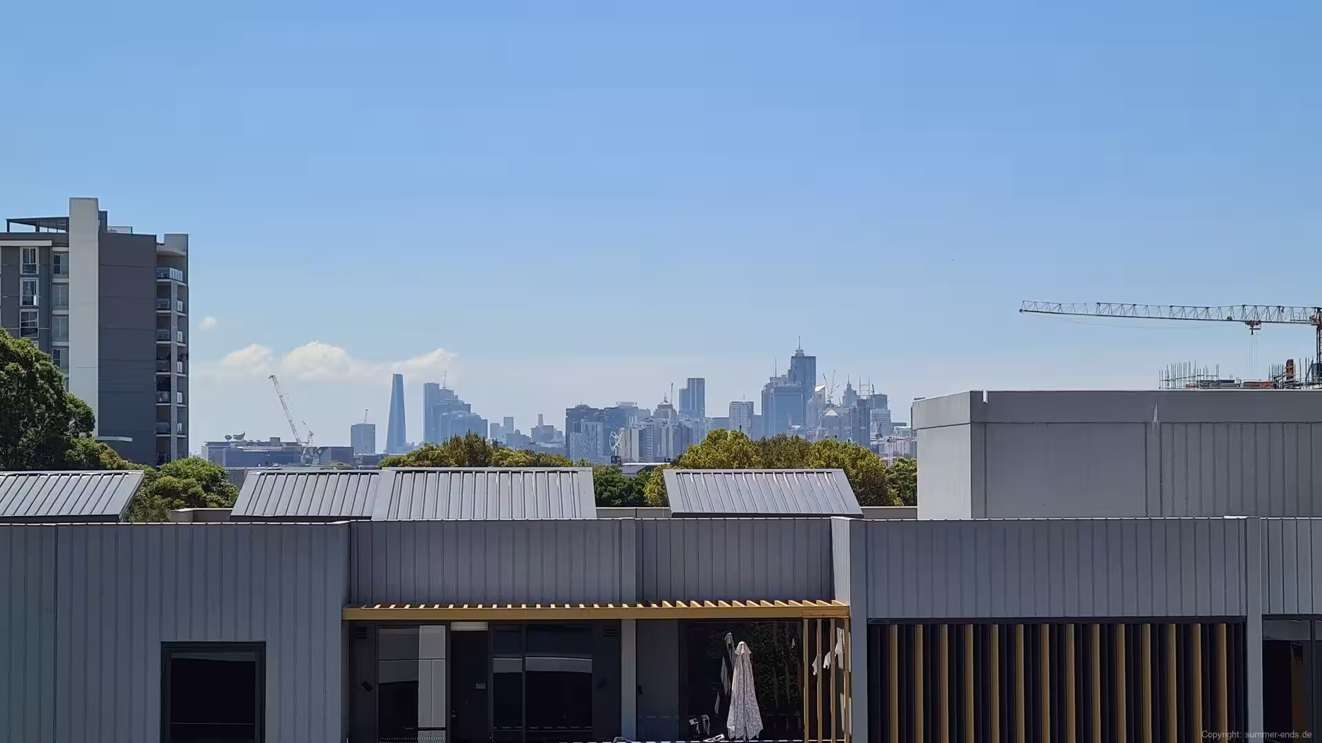 Grey rooftops give way to a dense high-rise skyline with construction cranes.