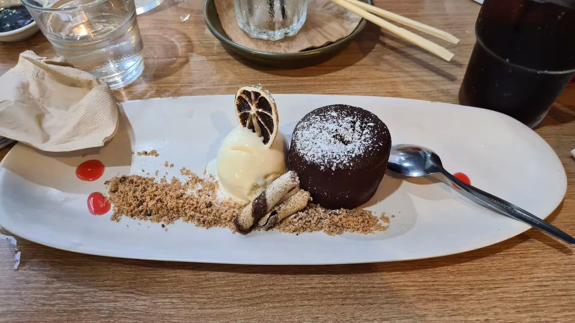 A warm chocolate fondant beside a scoop of vanilla gelato and a dried citrus slice.