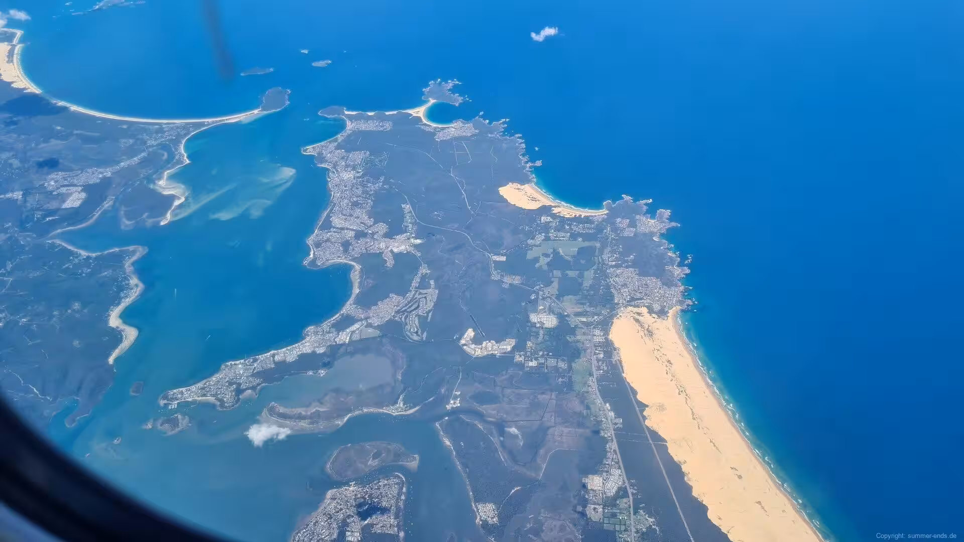 Turquoise lagoons and sandy spits stretch along a coastline seen from the air.