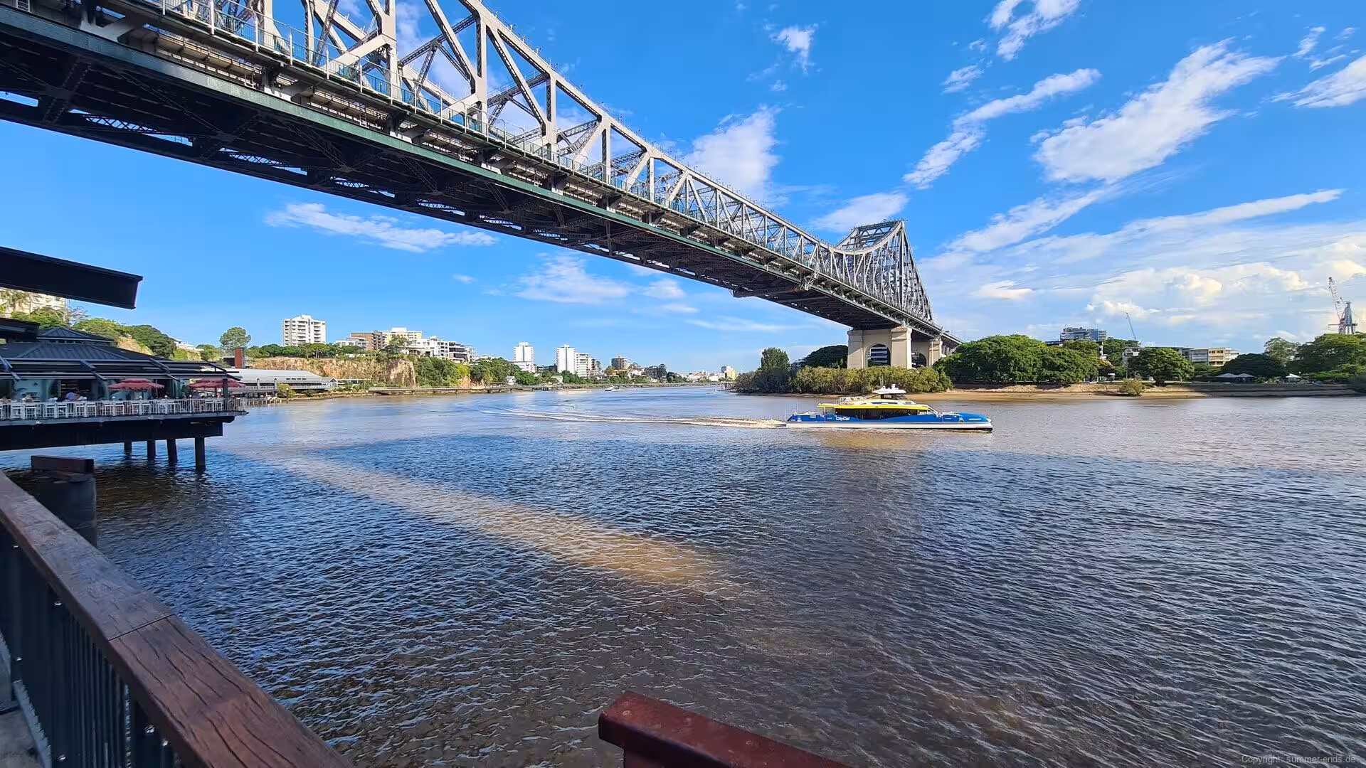 The green steel cantilever bridge spans a wide river on a bright day.