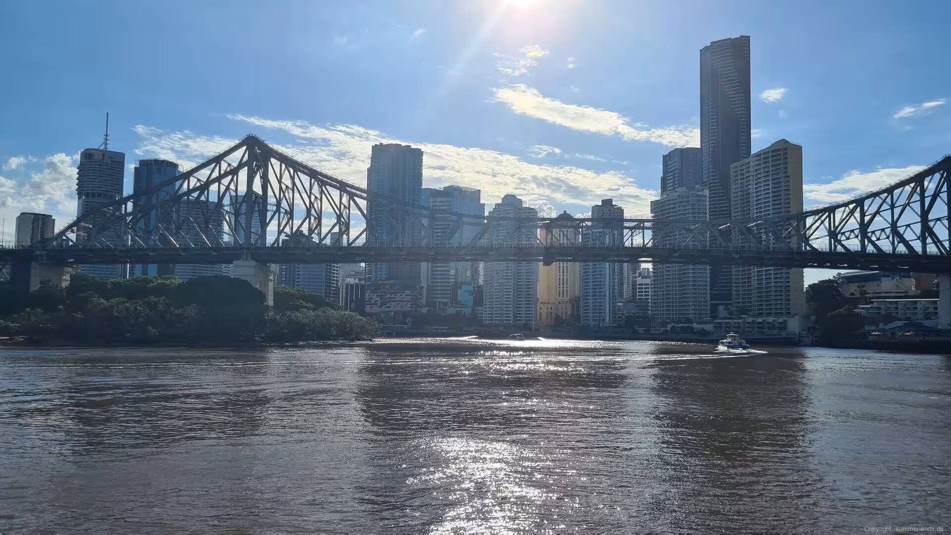 Sunlight glints off the river as the bridge frames a bright skyline.