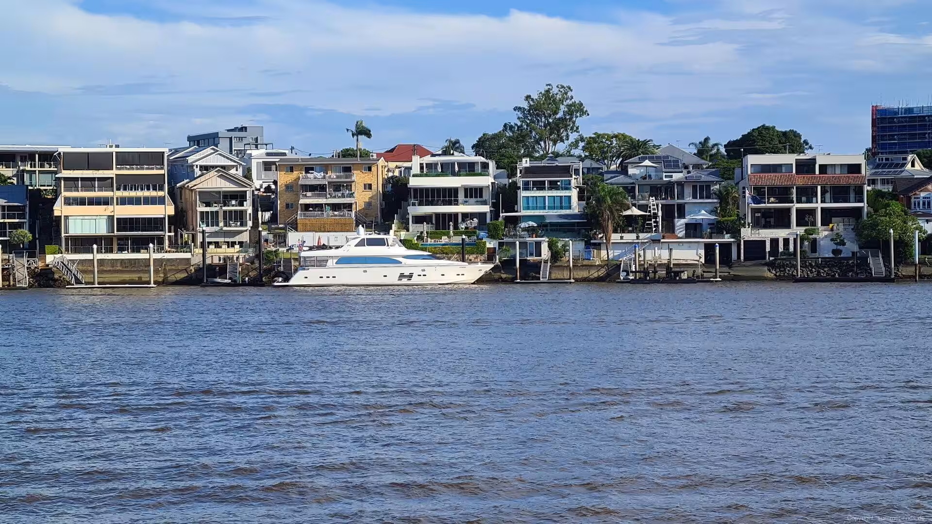 Waterfront homes line the bank with a yacht moored at the pier.