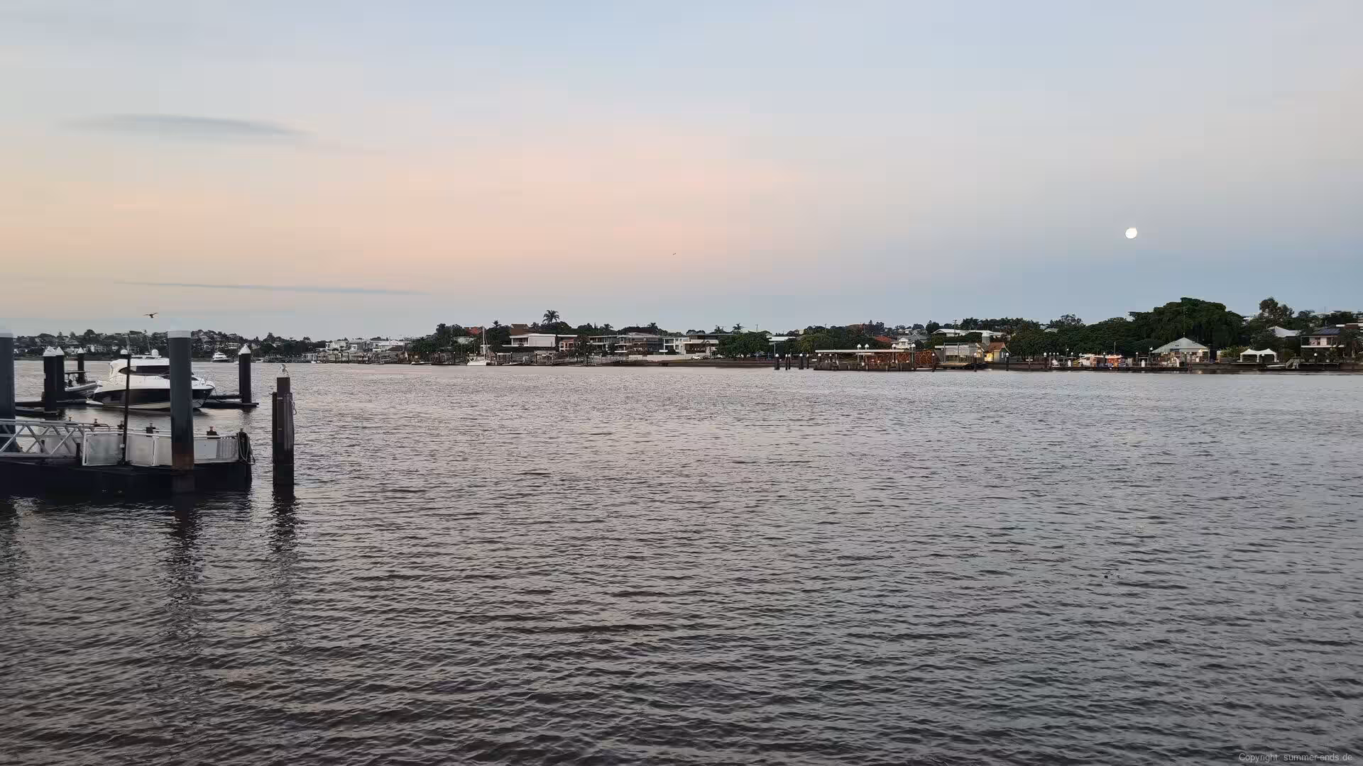 Pastel skies and a distant moon above still, dark water.