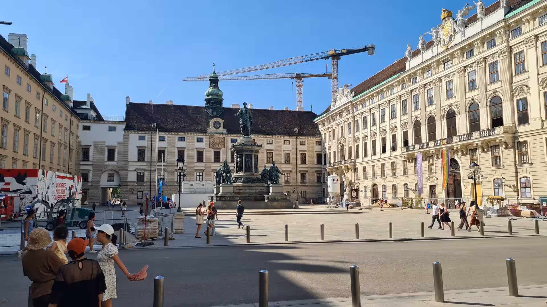 An equestrian monument stands in a Vienna palace courtyard surrounded by historic facades and a crane.
