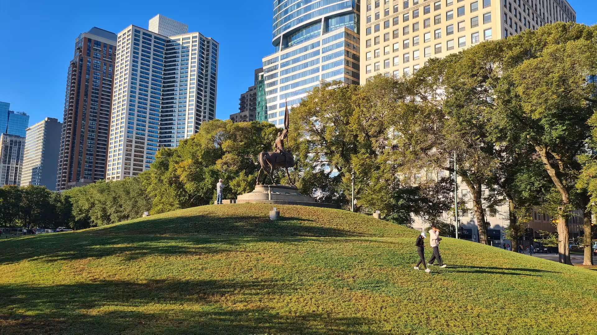 Historic equestrian statue on a grassy hill in Lincoln Park with Chicago skyscrapers rising in the background.