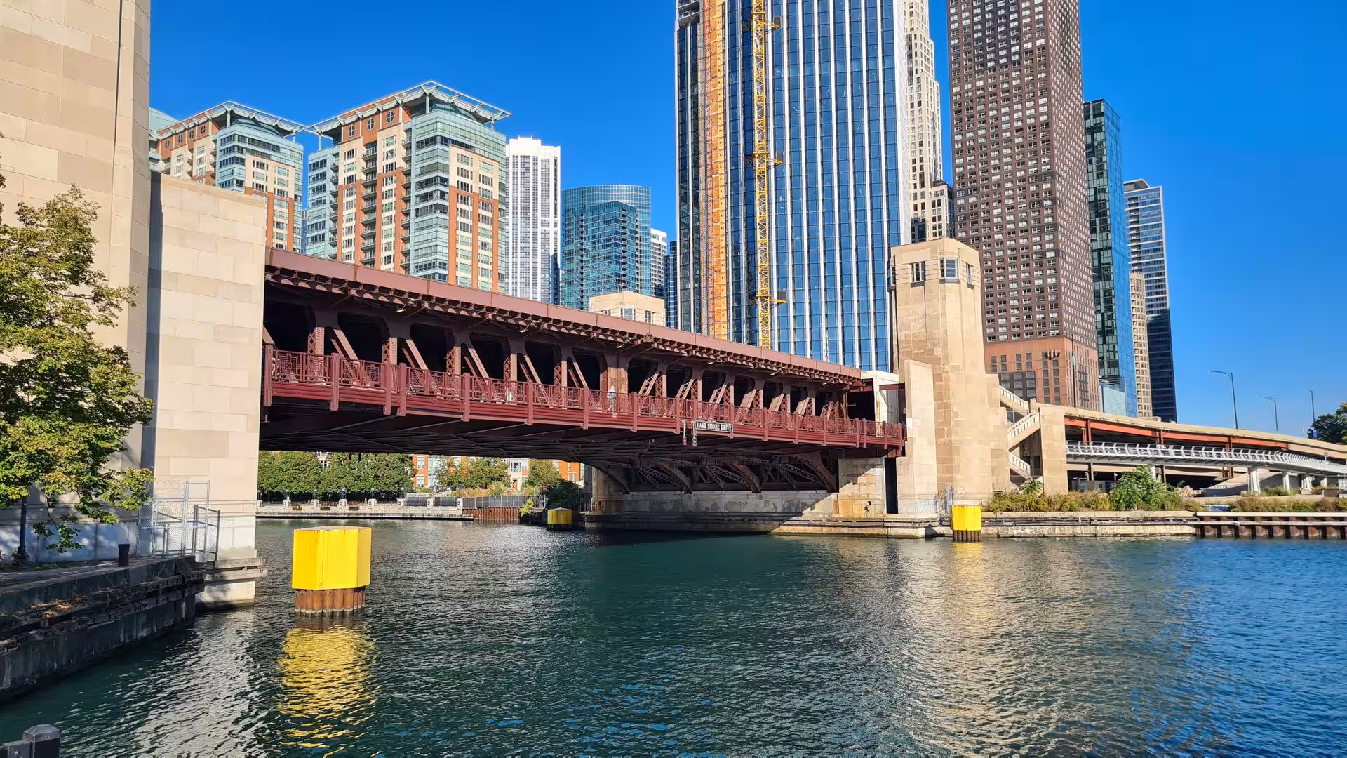Steel bridge spanning the Chicago River with modern skyscrapers and waterfront buildings in downtown Chicago.