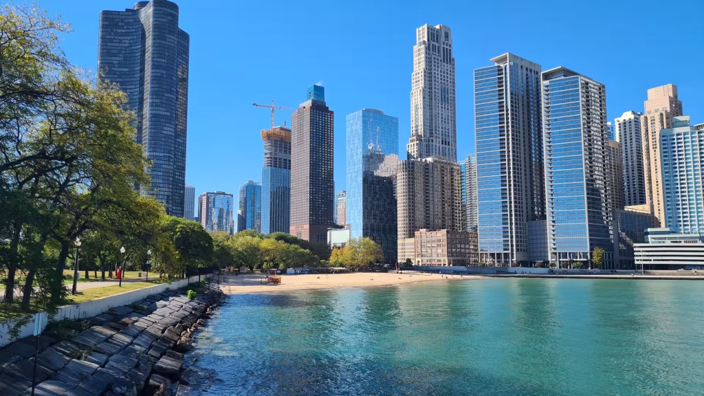 Chicago skyline rising above the shoreline of Lake Michigan with modern skyscrapers, a sandy beach, and turquoise water.