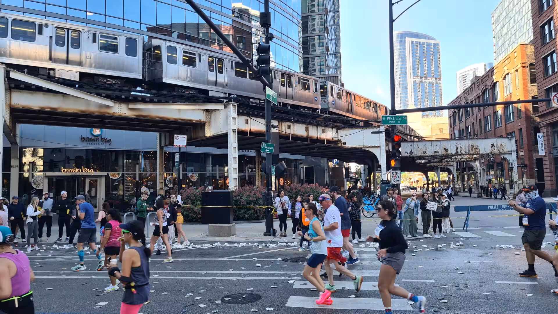 Participants in a Chicago road race running through downtown streets beneath an elevated CTA train track in the River North neighborhood.