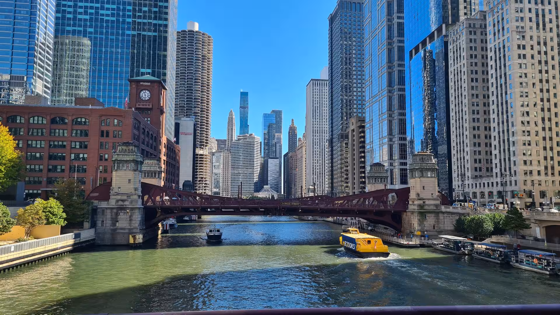 View along the Chicago River featuring the historic State Street Bridge, river traffic, and the downtown skyline on a clear day.