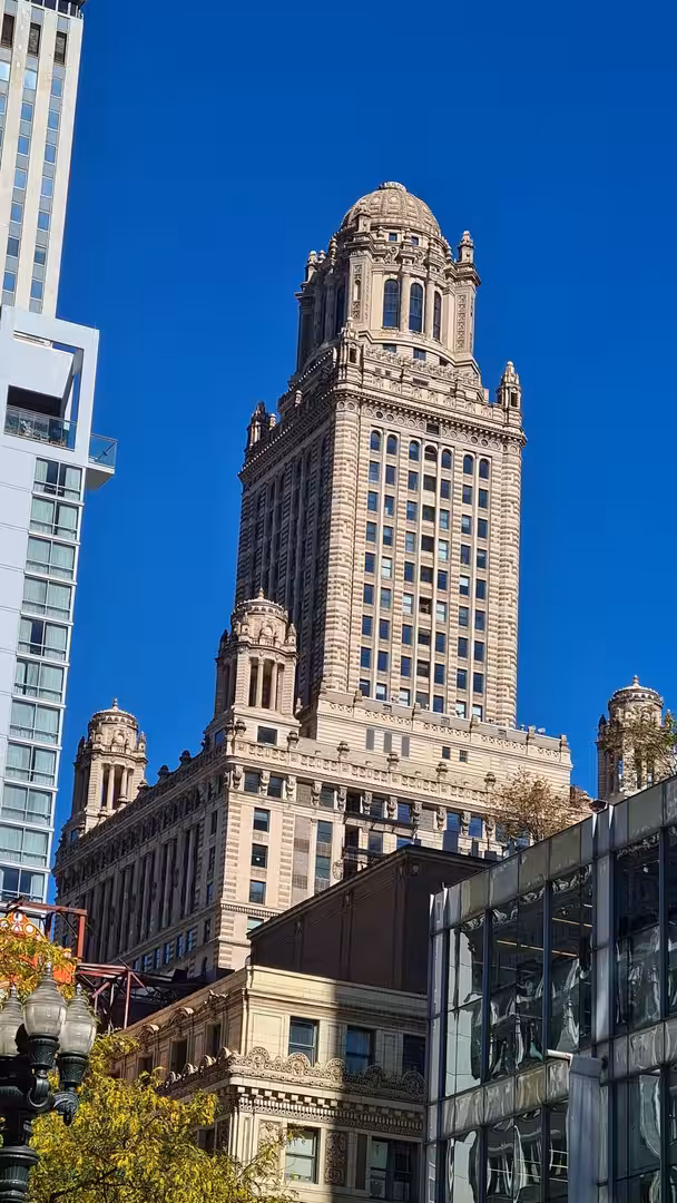 View of the historic Chicago Tribune Tower rising above surrounding buildings in downtown Chicago under a clear blue sky.