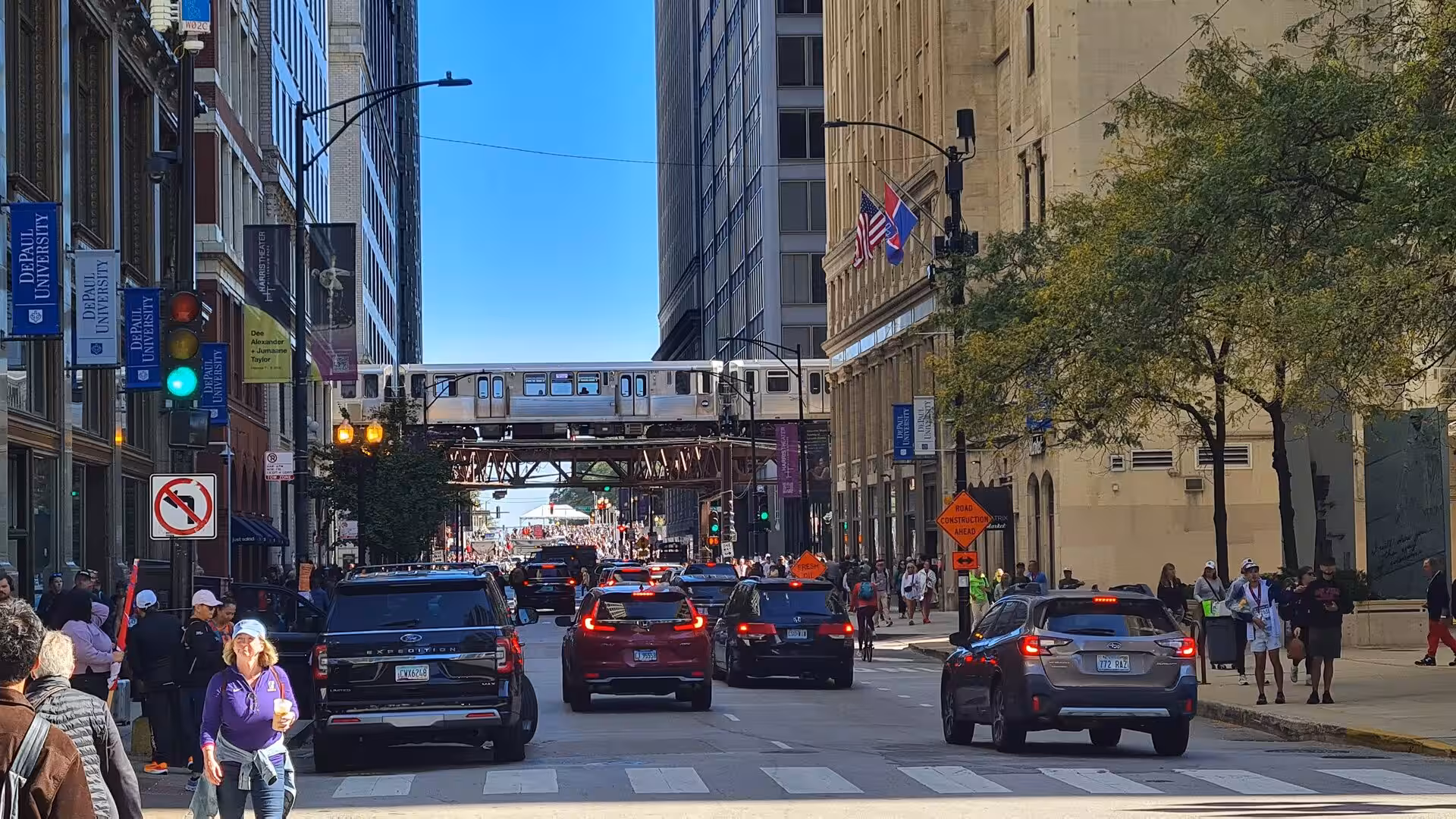 Busy street in downtown Chicago with cars, pedestrians, and a CTA elevated train crossing between tall buildings in the Loop district.