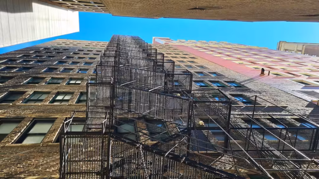 Upward view of tall brick buildings in downtown Chicago featuring stacked black metal fire escapes against a bright blue sky.