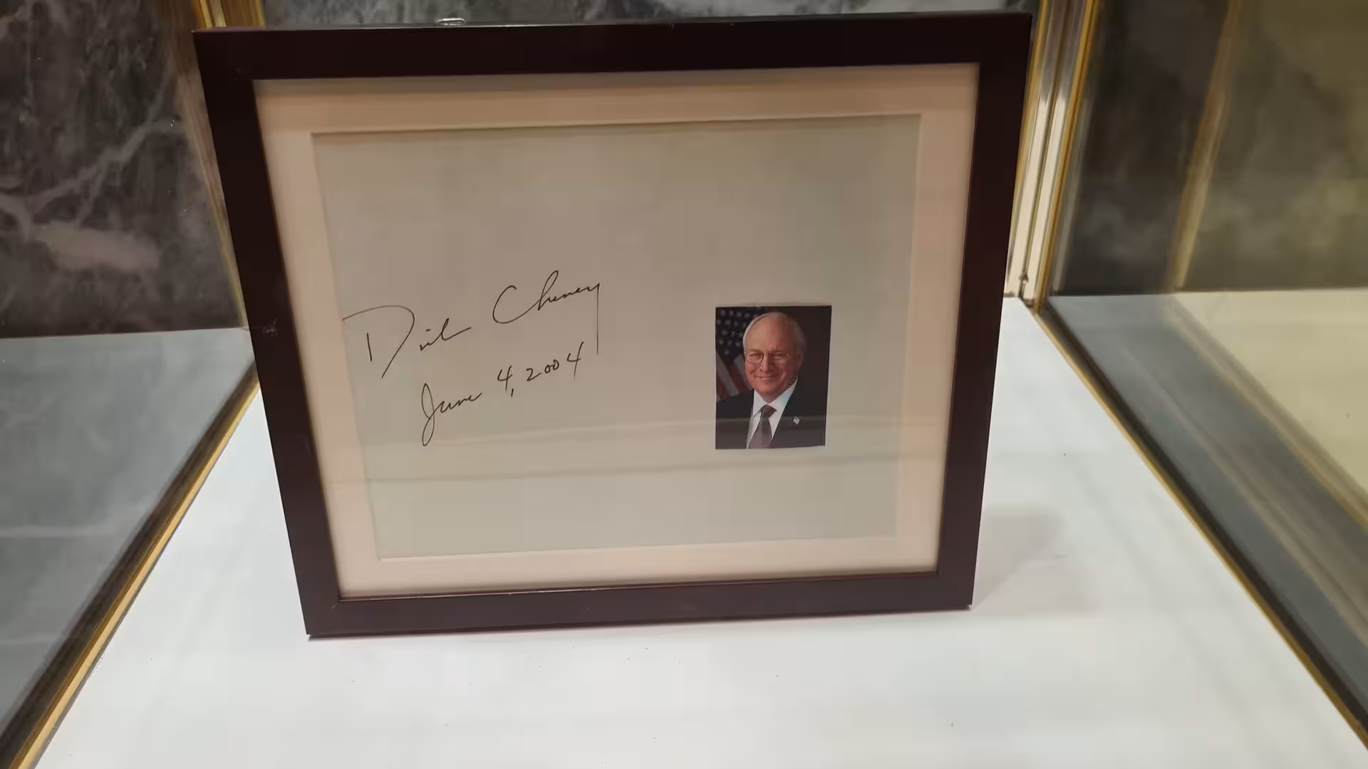 Framed signature display featuring a handwritten signature, dated inscription, and portrait photograph presented in a glass showcase.