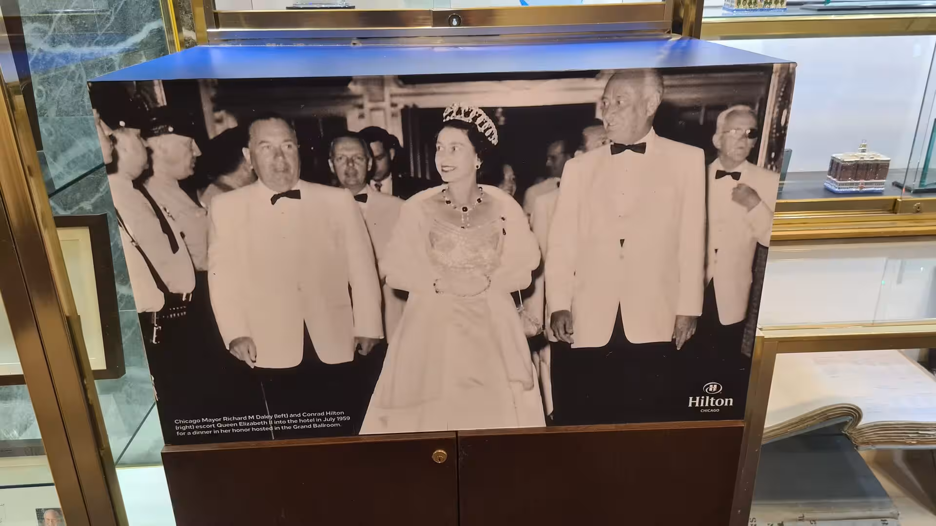 Historic black-and-white photograph showing Queen Elizabeth II arriving at a formal event alongside local dignitaries at a Chicago hotel.