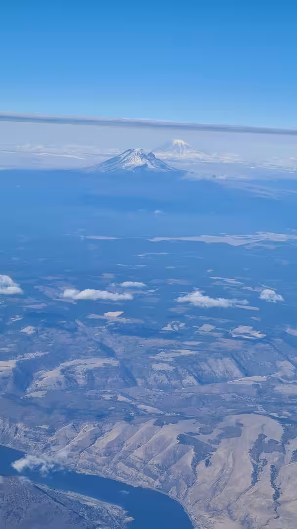 Snow-covered volcanic peaks rising above clouds and rugged landscapes in the Pacific Northwest