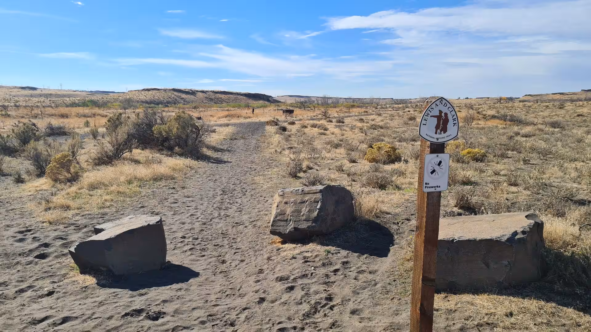 Sandy desert trail with Lewis and Clark sign in a dry shrubland landscape under blue skies