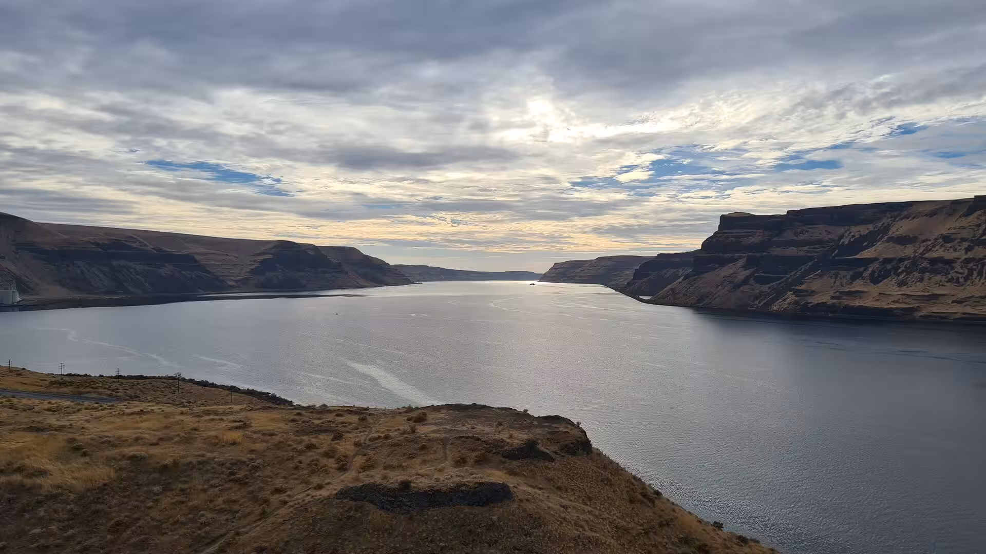 Wide canyon of the Columbia River bordered by dark basalt cliffs under a dramatic cloudy sky