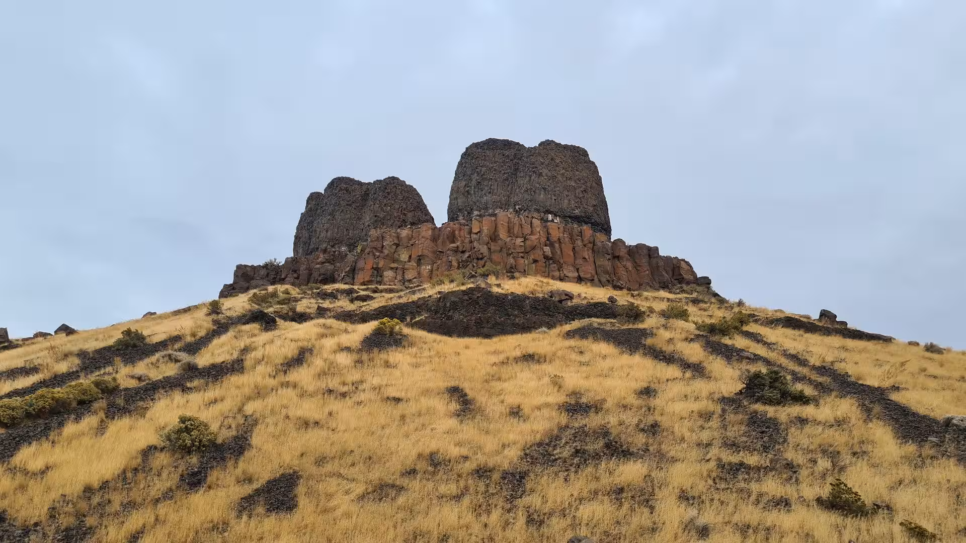 Twin basalt rock formations rising above dry grass-covered hills in the Columbia Plateau