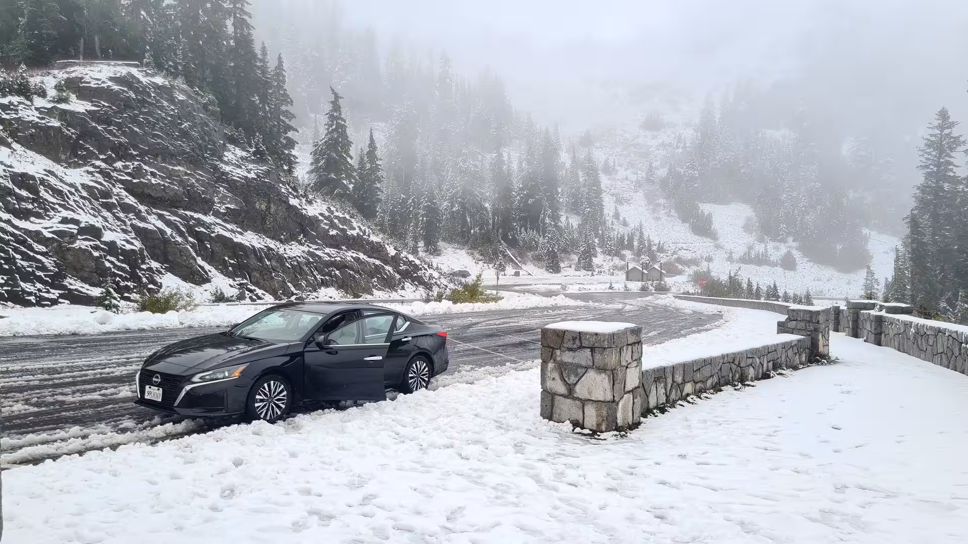 Snow-covered mountain pass with evergreen forests and a car during a winter storm in the Cascades