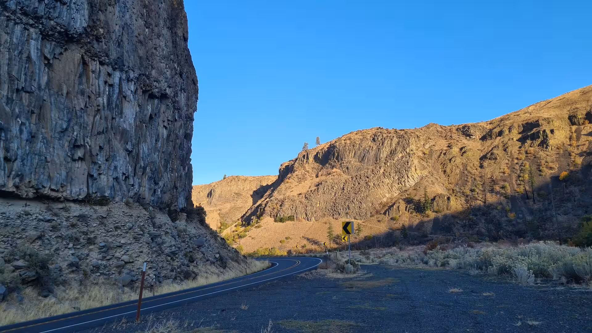 Winding road passing towering basalt cliffs and volcanic canyon walls beneath a clear blue sky