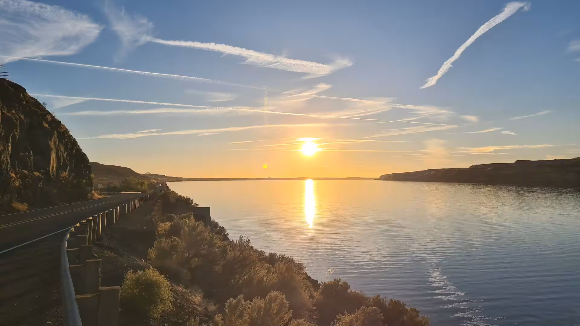 Golden sunset reflecting across the Columbia River beside a canyon road and basalt cliffs in eastern Washington