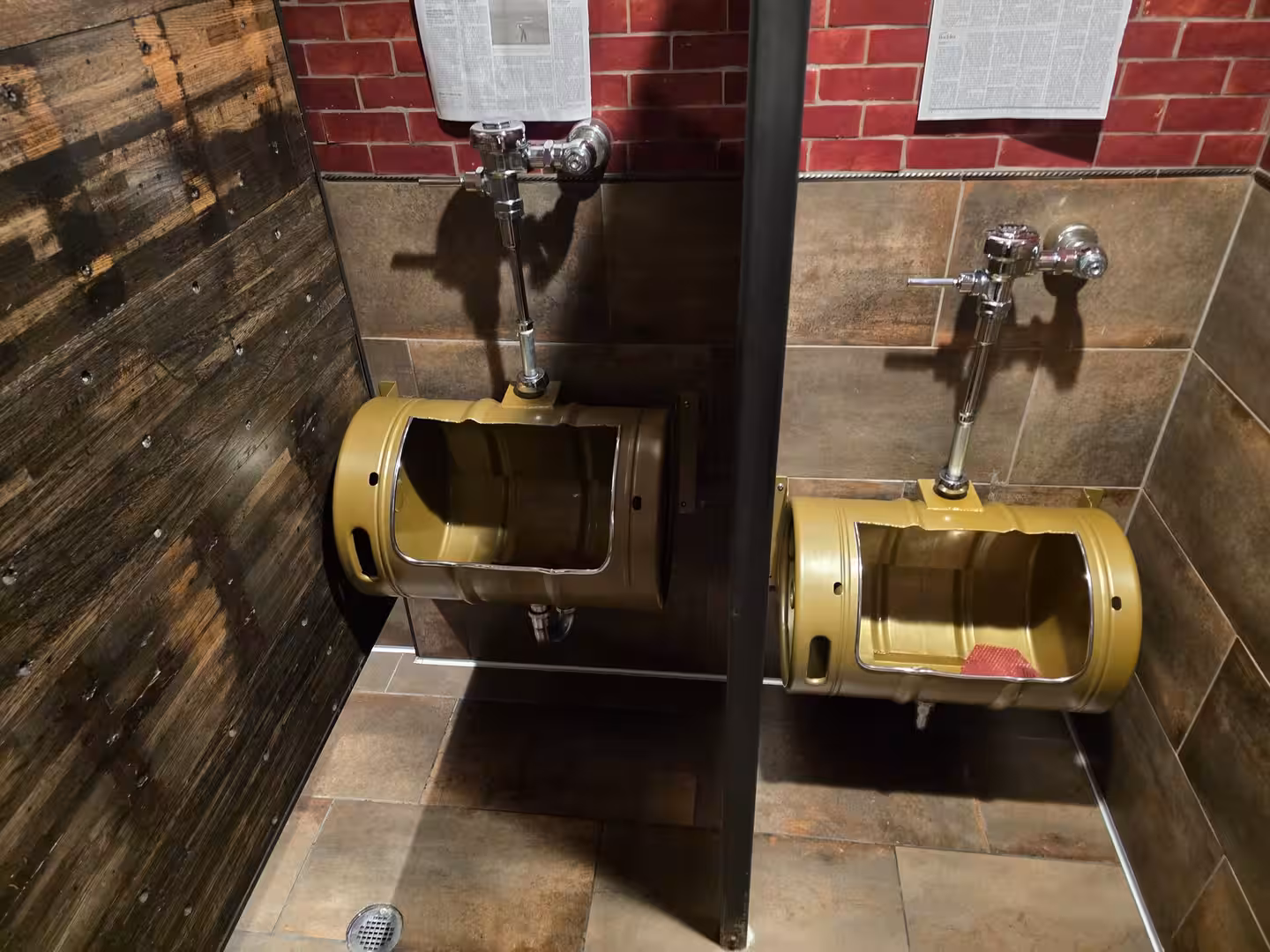 Rustic restroom with industrial barrel-style urinals and red brick wall tiles