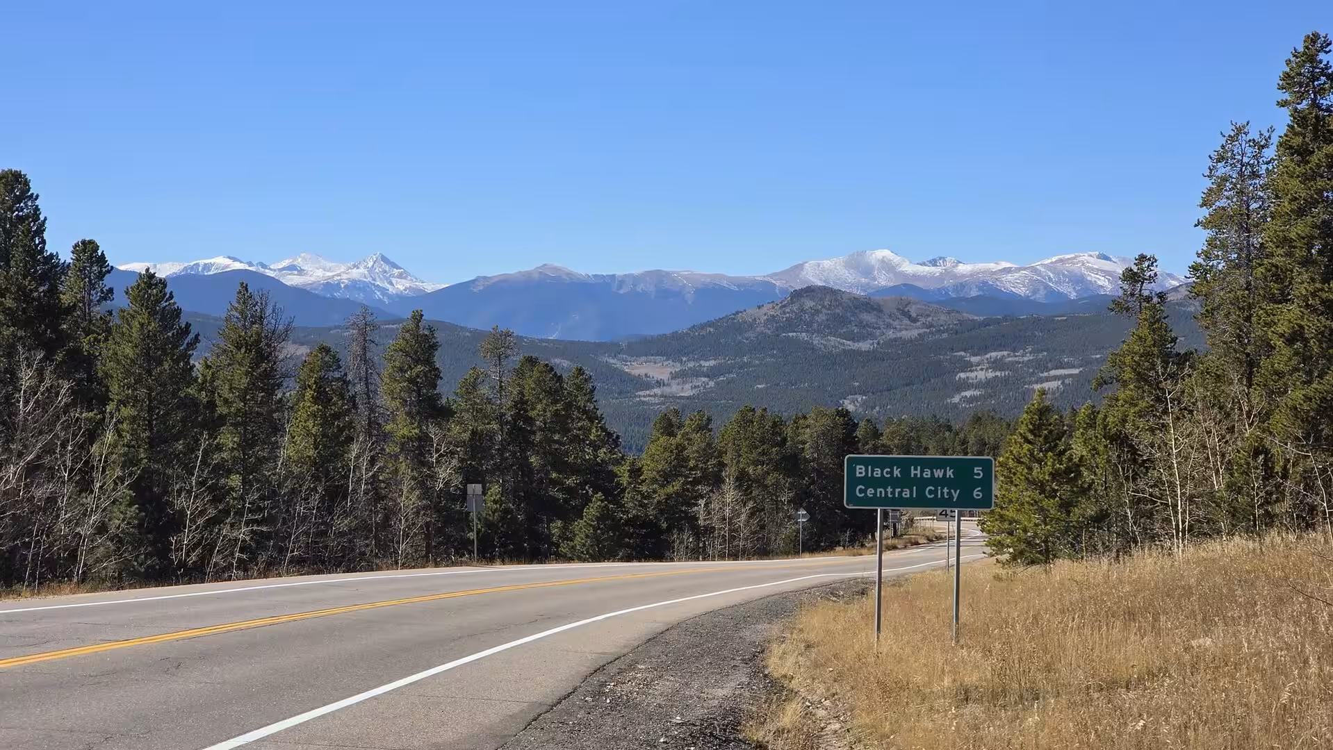 Mountain road through evergreen forest with snow-covered Rocky Mountains near Black Hawk and Central City, Colorado