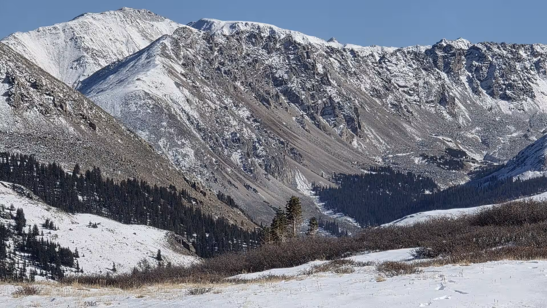 Snow-covered mountain peaks and rugged alpine ridges beneath a clear blue sky in the Colorado Rockies