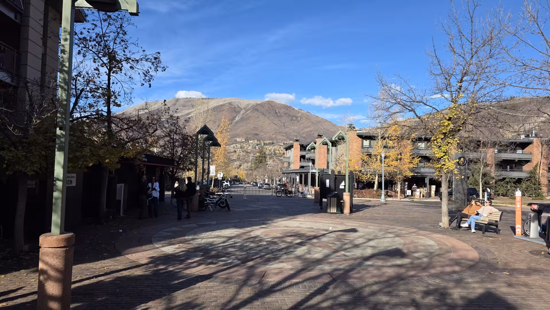 Pedestrian plaza in Aspen with mountain views, autumn trees, and alpine resort buildings under a blue sky
