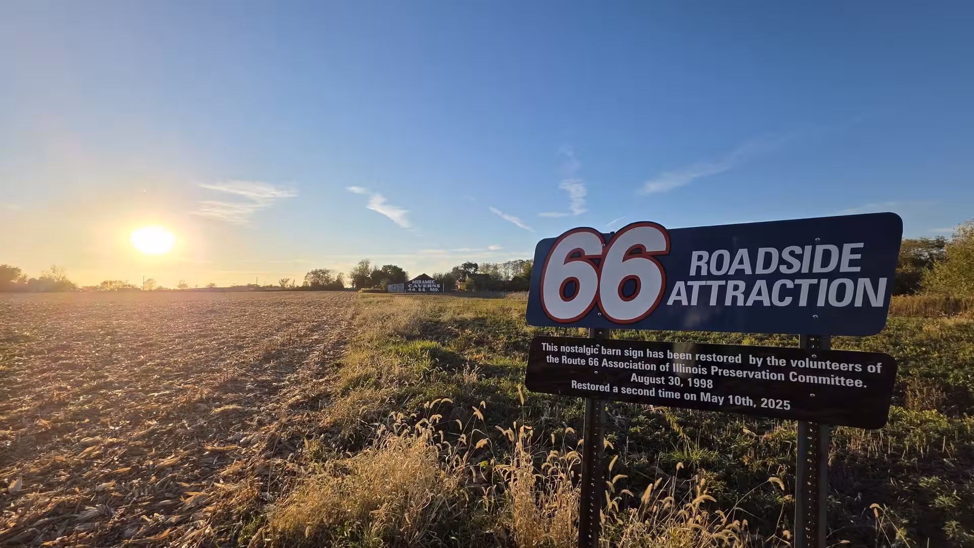 Route 66 roadside attraction sign beside farmland at sunset in rural Illinois.