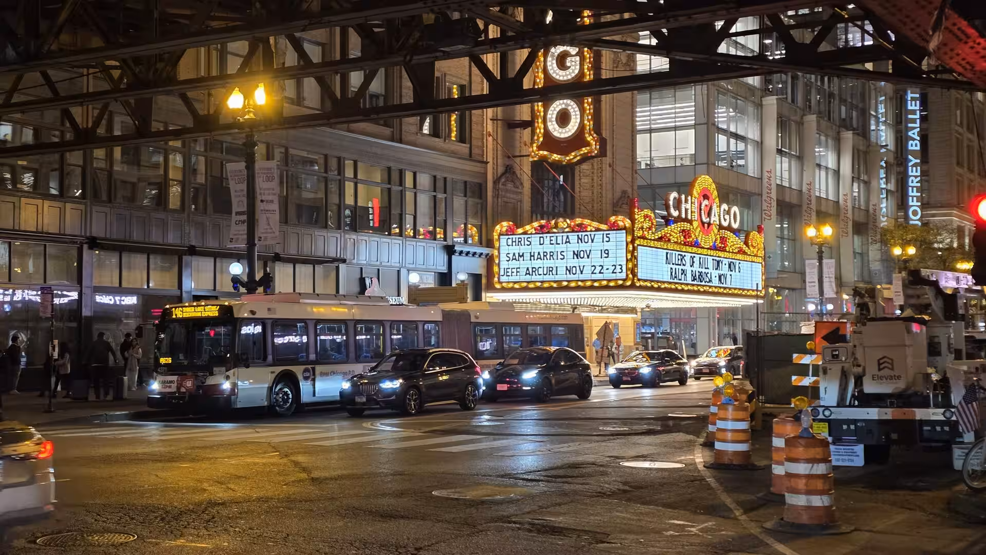 Nighttime street scene in downtown Chicago with the illuminated Chicago Theatre marquee beneath elevated train tracks