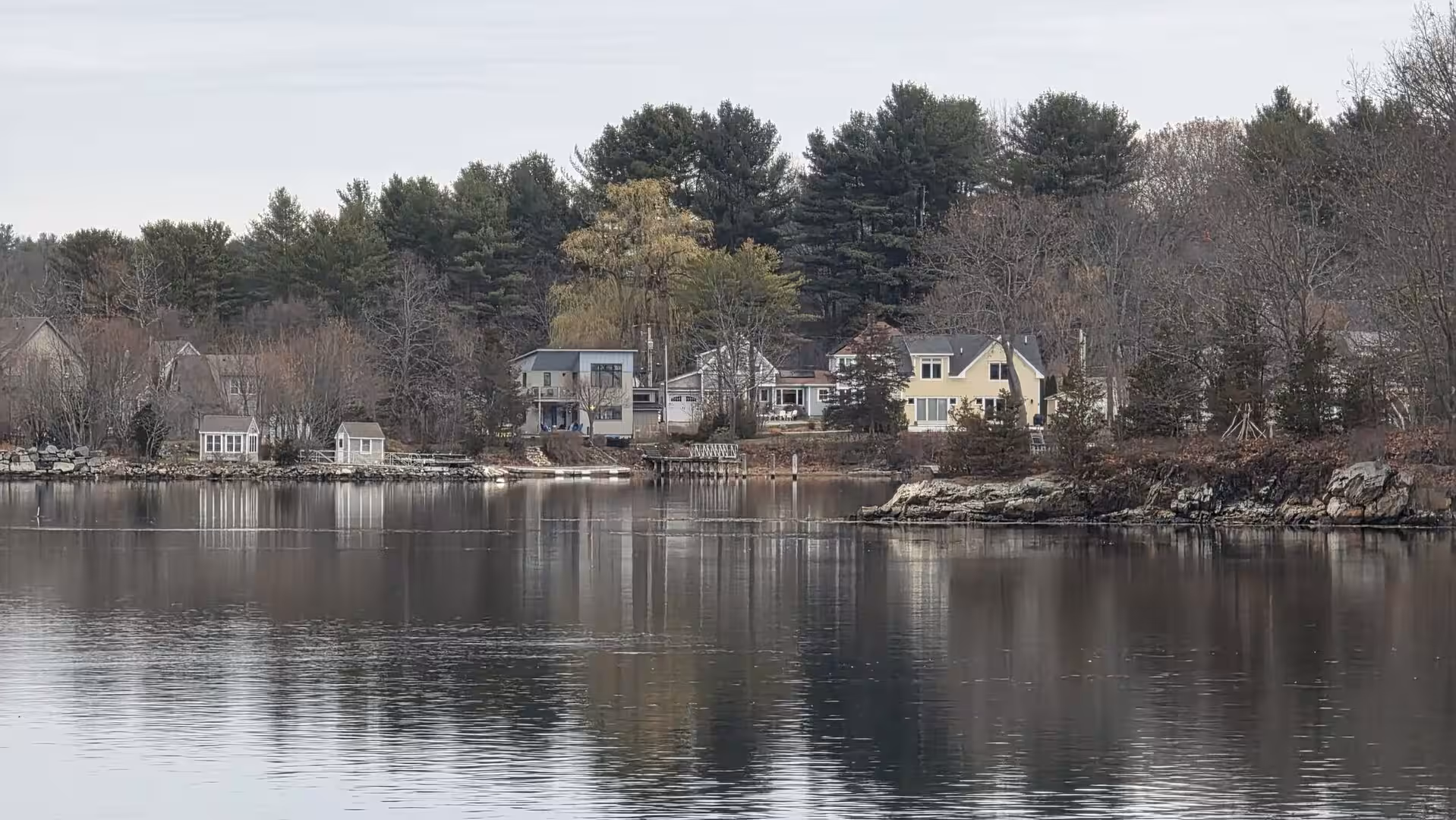 Quiet wooded shoreline with waterfront homes reflected in calm inlet waters.