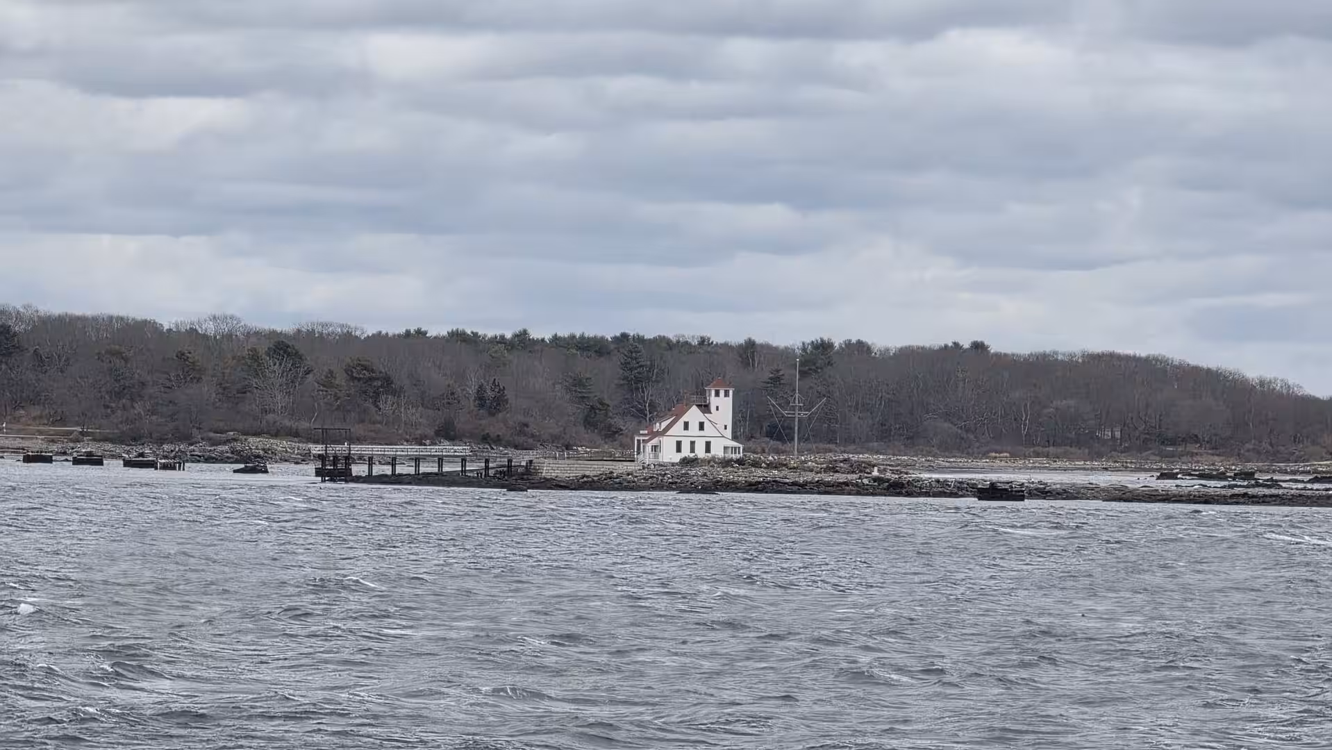 Small white coastal lighthouse building on a rocky island surrounded by choppy Atlantic waters beneath overcast skies.