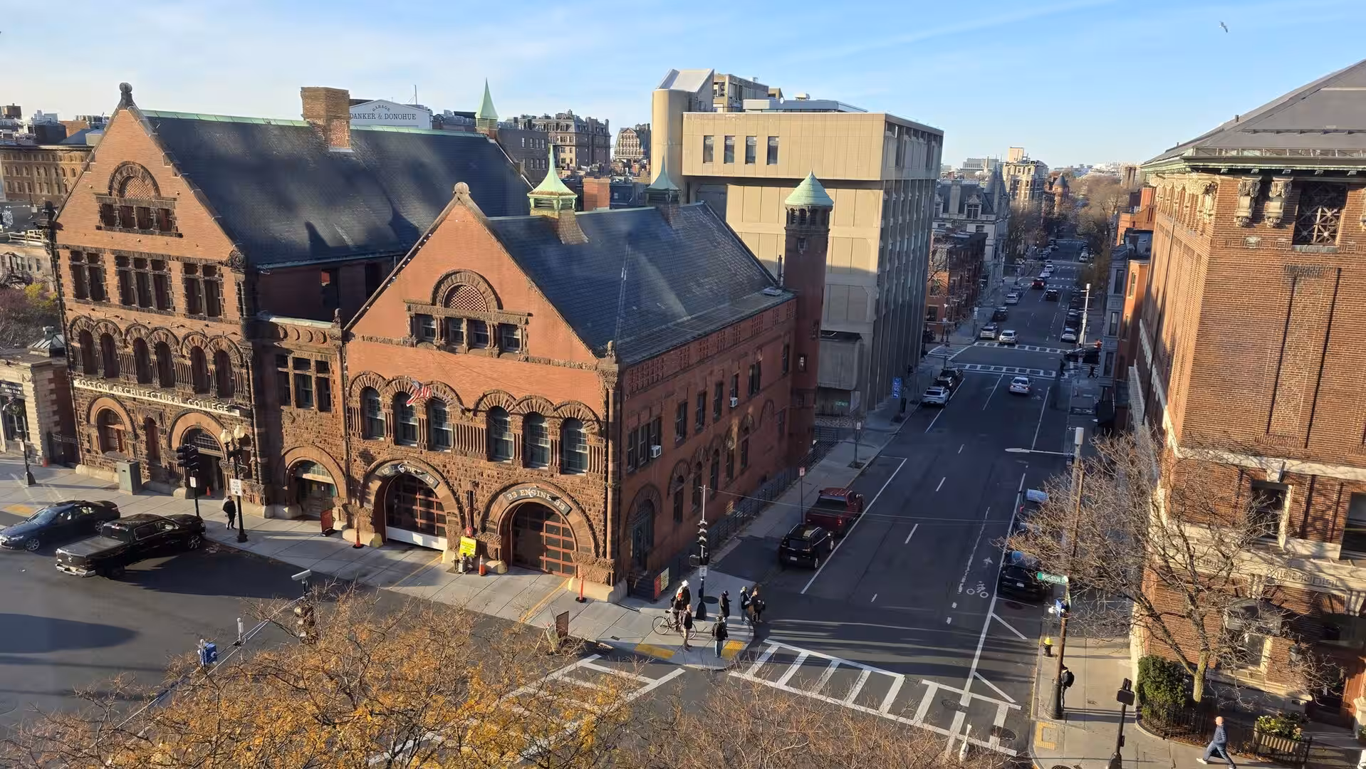 Historic red-brick Boston Architectural College building beside a quiet city street in warm afternoon sunlight.