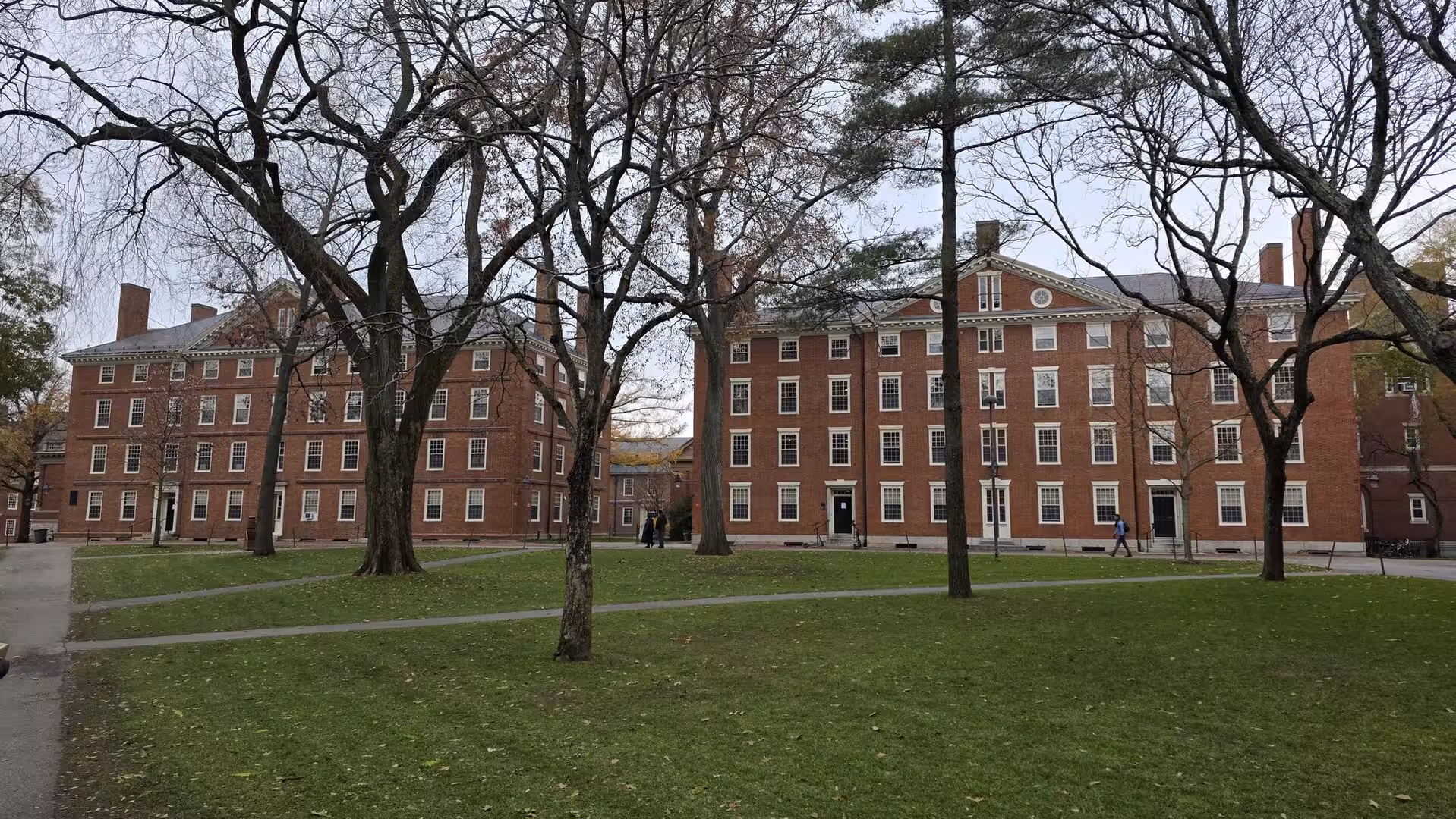 Historic red-brick university dormitory buildings surrounded by leafless trees and green lawns on a quiet campus courtyard.