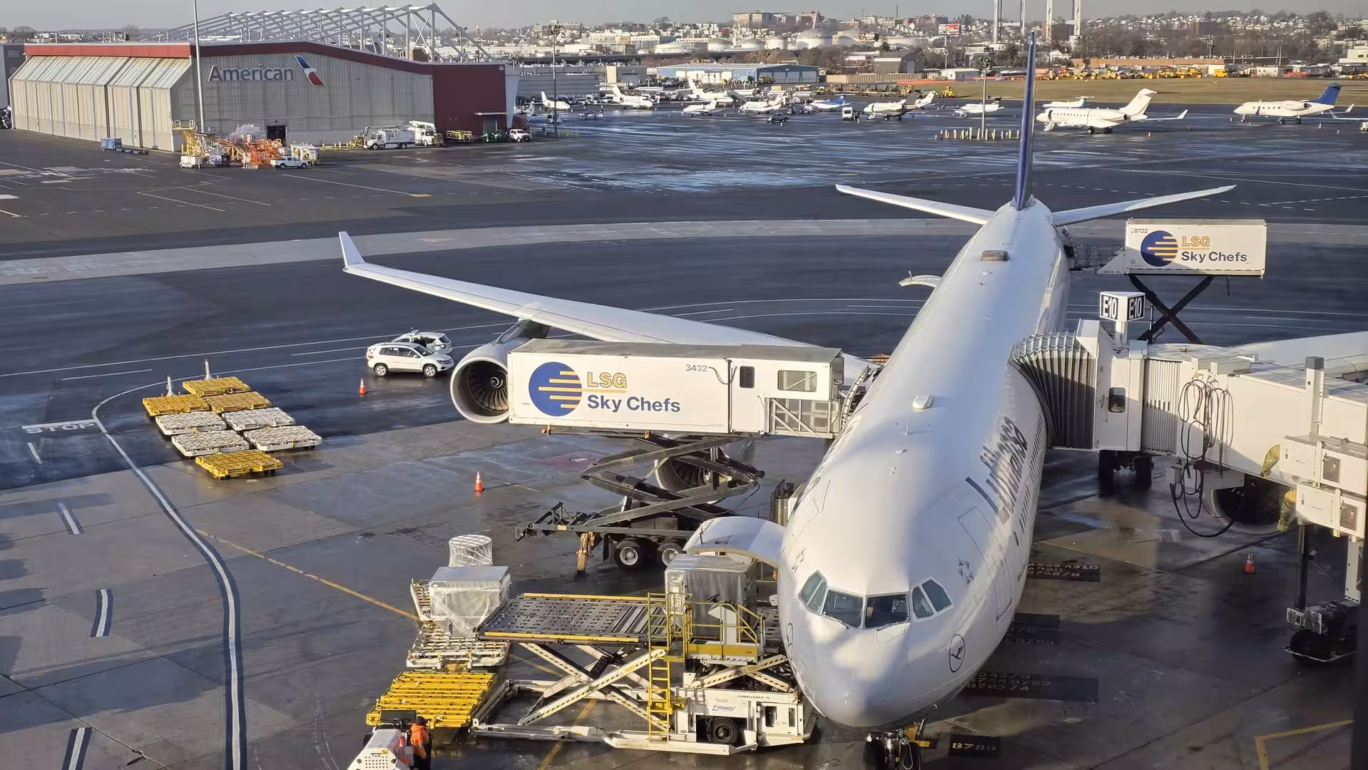 Lufthansa widebody aircraft parked at an airport gate during catering and cargo loading operations on a clear winter afternoon.