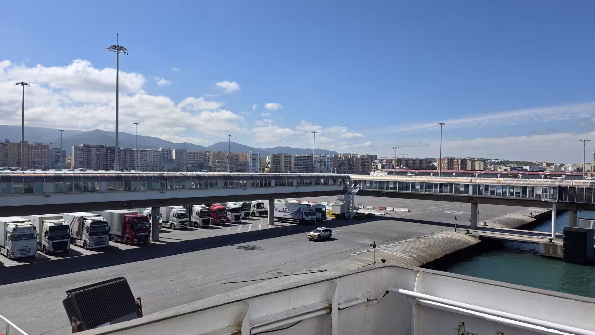 View from a ferry departing Algeciras with the terminal and parked trucks visible ashore.