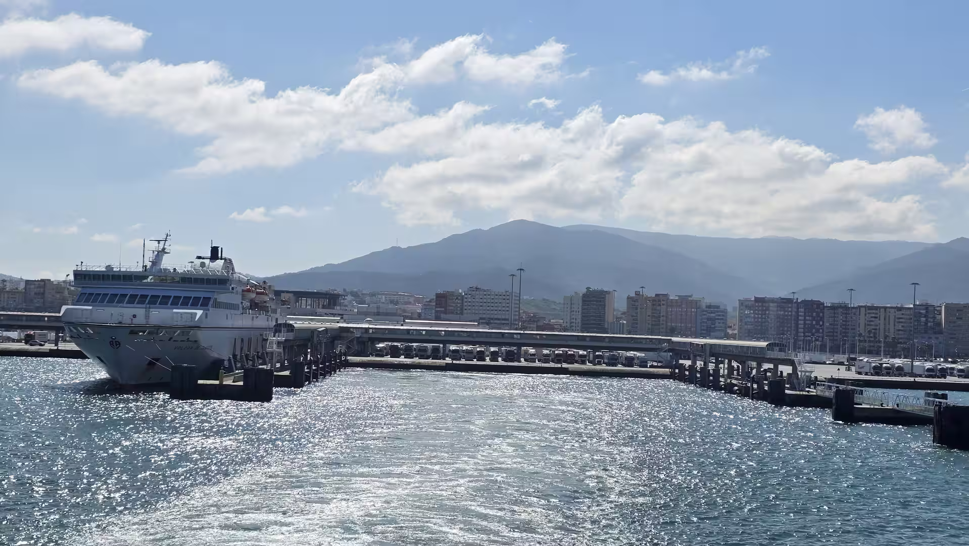 View from a ferry departing Algeciras with harbor facilities and mountains in the background.