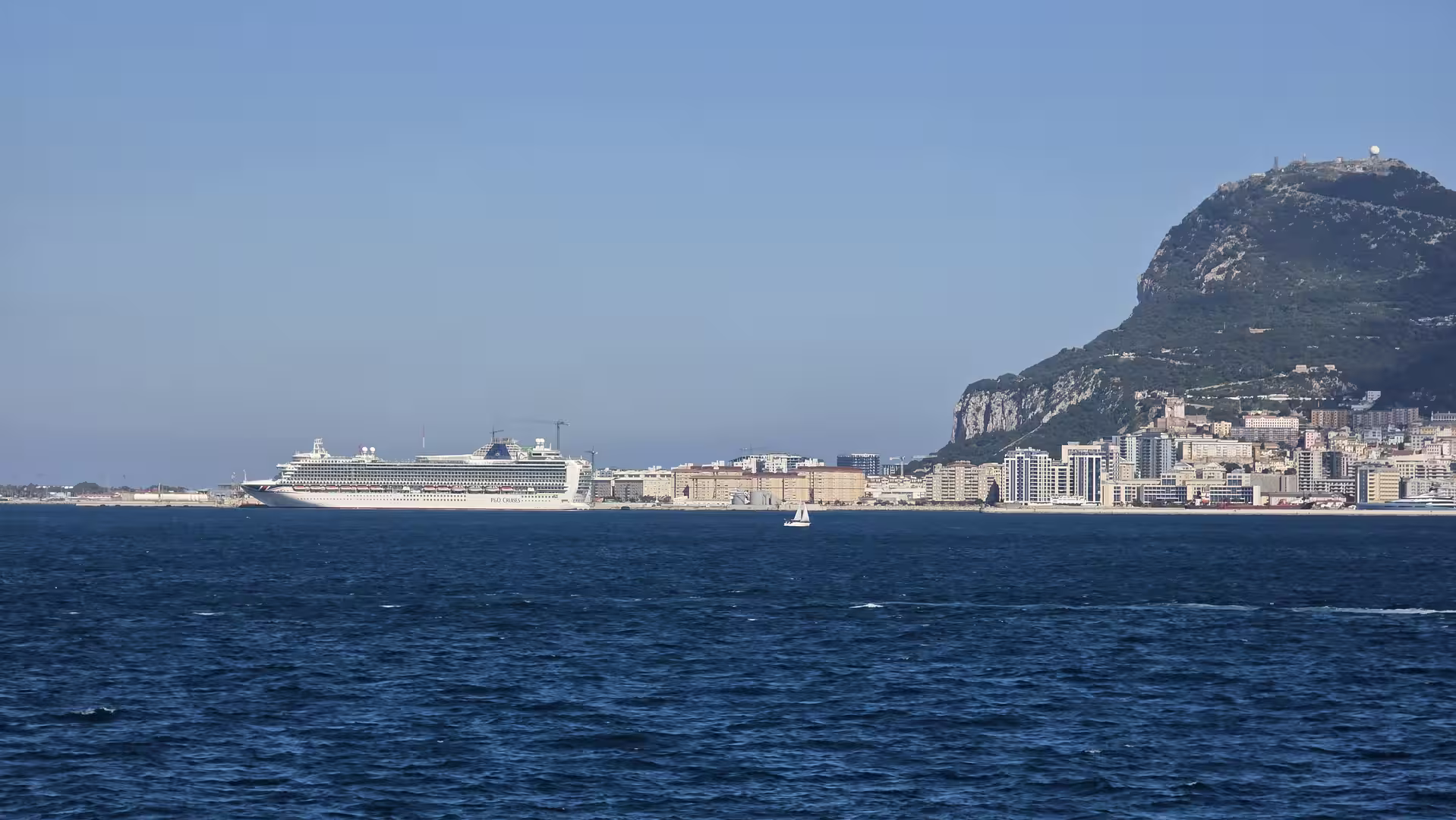 Cruise ship sailing along the coast of Gibraltar with the Rock towering above the city.