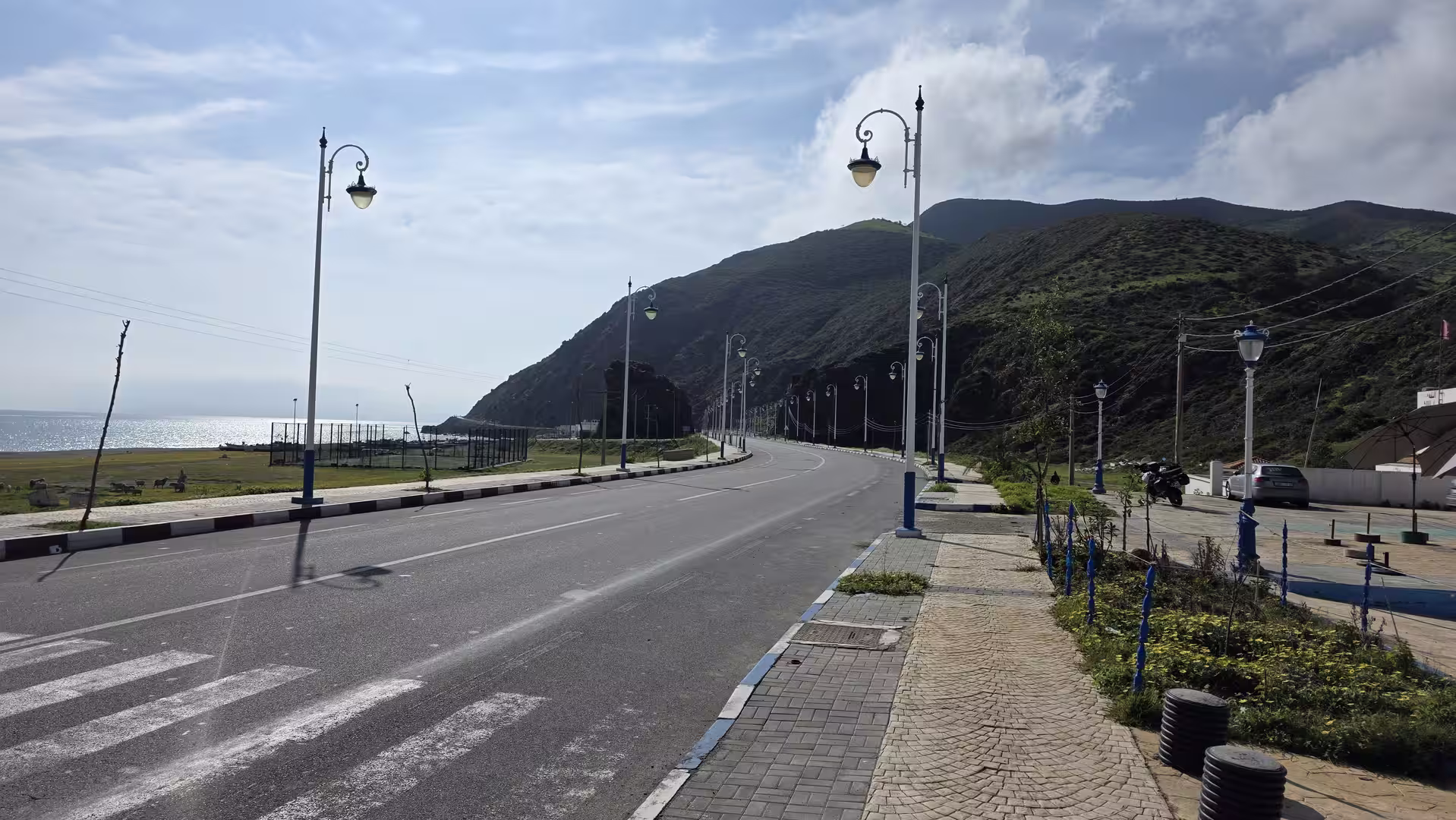 Scenic coastal road along the Mediterranean shoreline near Fnideq with mountains rising above the sea.